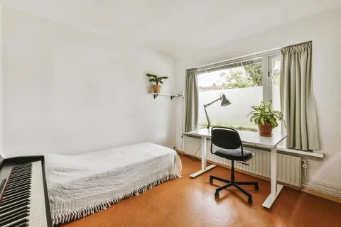 A bedroom with a bed desk and a window Stock Photos