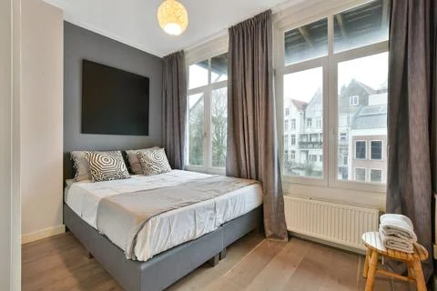 A bedroom with a large bed and a large window Stock Photos