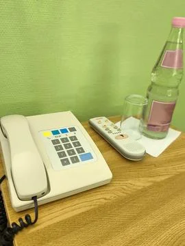 A bedside table in a room or hotel with a telephone, remote control, and a 스톡 사진