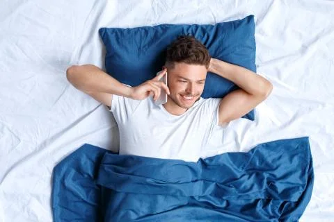 Bedtime. Guy lying on bed top view talking on phone smiling cheerful Stock Photos