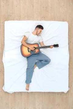 Bedtime. Guy lying on bed top view palying guitar singing excited Stock Photos