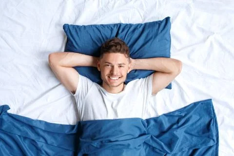 Bedtime. Guy lying on bed top view hands under head smiling relaxed Stock Photos