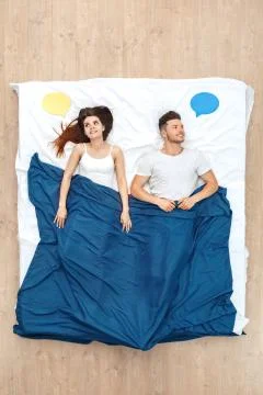 Bedtime. Young couple lying under blanket on bed top view with speech bubble Stock Photos