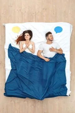 Bedtime. Young couple lying under blanket on bed top view with speech bubble Stock Photos