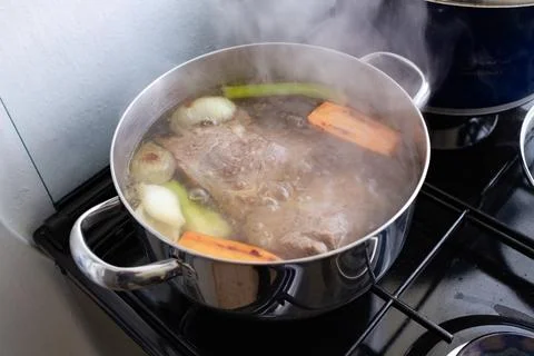 Beef and vegetables simmer in a steaming pot on a gas stove for broth. Stock Photos