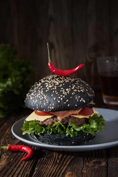 Beef burger with chilli pepper with black bread on rustic wooden background. Stock Photos