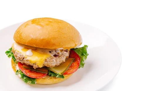 Beef cheeseburger with bun, lettuce, tomato, pickles on plate Stock Photos
