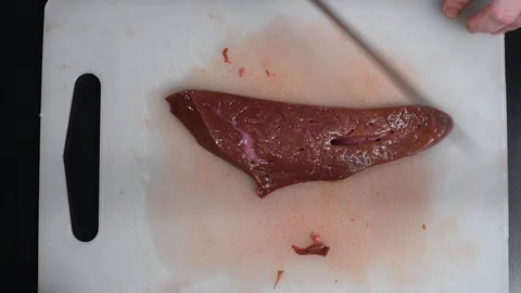 Beef liver on the table cut with a knife on a white cutting Board Stock Footage 103154519