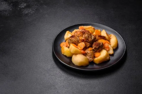 Beef meat and vegetables stew on a black plate with roasted potatoes Stock Photos