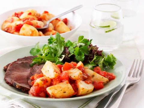 Beef with a side of tomatoes and potatoes and a mixed leaf salad 스톡 사진