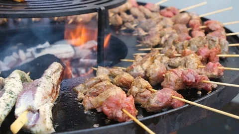 Beef skewers cook over fire. Duck breasts roast beside them on a brazier. Stock Footage 344381535