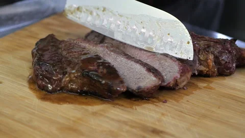 Beef steak is cut with a large knife into appetizing pieces on a wooden board Stock Footage 144703152