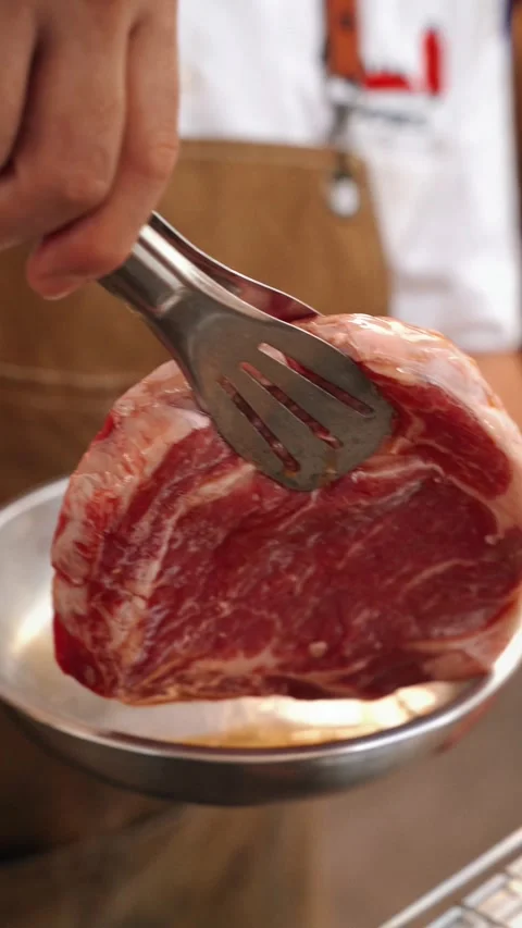 Beef steak dipped in sauce and placed on smoky grill with tongs Stock Footage 314629595