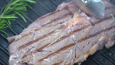 Beef steak on the grill is lifted with forceps and turned over to the other side Stockbeeldmateriaal 75057089