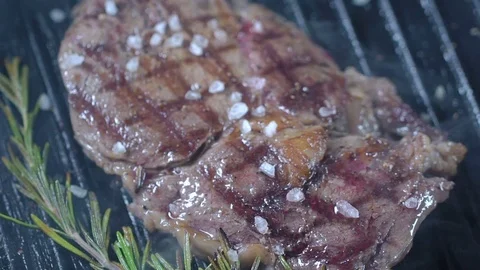 Beef steak on the grill is sprinkled with large sea salt and black pepper . Slow Stock Footage 75240129