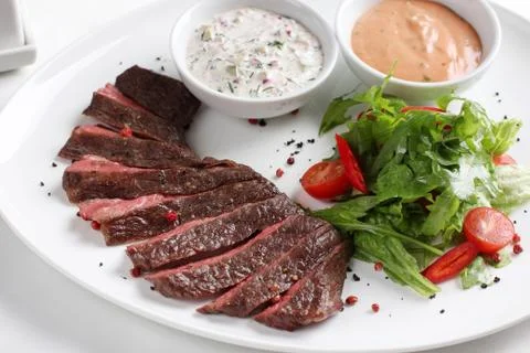 Beef steak, medium rare, with fresh vegetables, herbs and sauce on a white pl Stock Photos