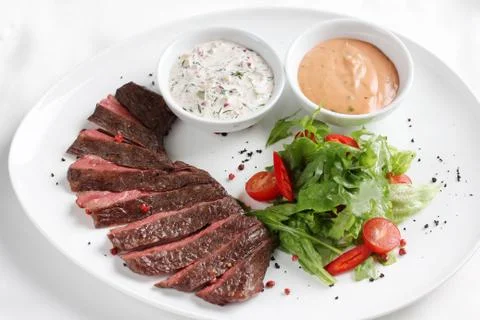 Beef steak, medium rare, with fresh vegetables, herbs and sauce on a white pl Stock Photos