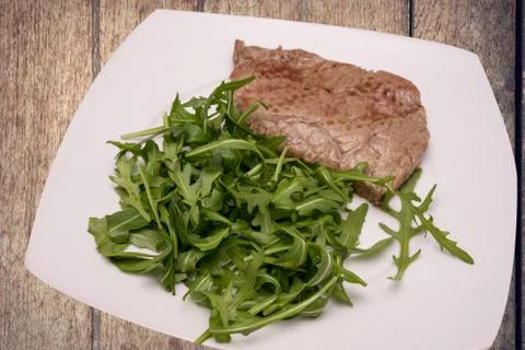 Beef steak with rocket garnish, on white plate Stock Photos