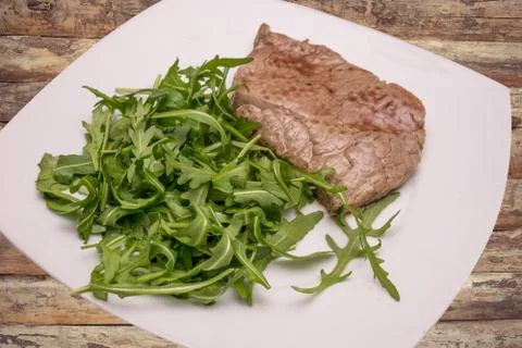 Beef steak with rocket garnish, on white plate Stock Photos