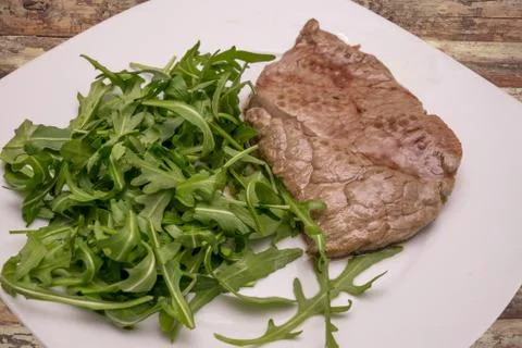 Beef steak with rocket garnish, on white plate Stock Photos