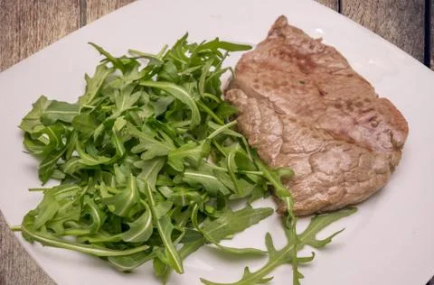 Beef steak with rocket garnish, on white plate Stock Photos