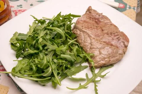 Beef steak with rocket garnish, on white plate Stock Photos