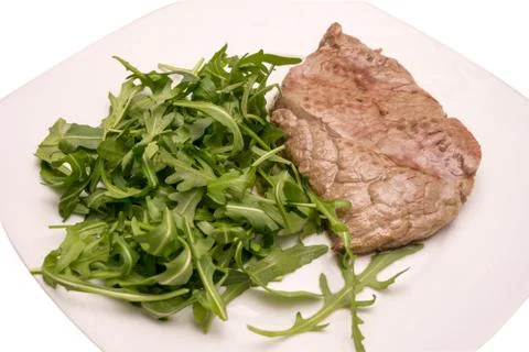 Beef steak with rocket garnish, on white plate Stock Photos