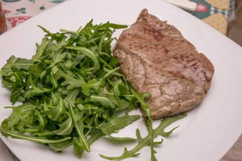 Beef steak with rocket garnish, on white plate Stock Photos