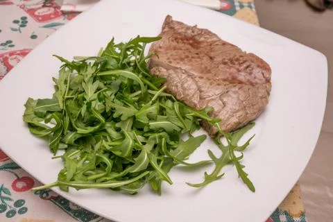 Beef steak with rocket garnish, on white plate Stock Photos