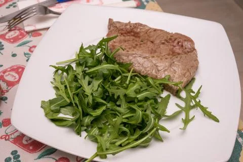 Beef steak with rocket garnish, on white plate Stock Photos
