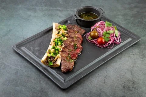 Beef steak with sugar bone, served with sauce and salad of onions, pomilors and Stock Photos