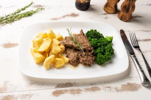 Beef stew with rustic potato and broccoli in a white plate on white wooden ta Stock Photos