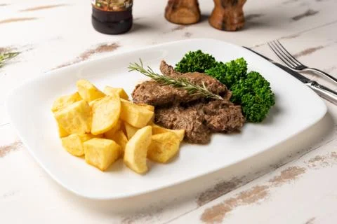 Beef stew with rustic potato and broccoli in a white plate on white wooden ta Stock Photos