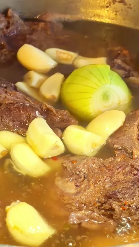Beef Stew With Whole Onion Potatoes and Garlic Cloves Simmering in Metal Pot Stock Footage 337240744