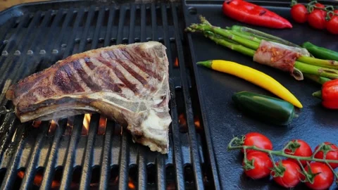 Beef T-Bone steak on the cooking grill with grilled vegetables. Slow motion. Stock Footage 271137387