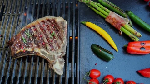 Beef T-Bone steak on the cooking grill with grilled vegetables. Slow motion. Stock Footage 273219333