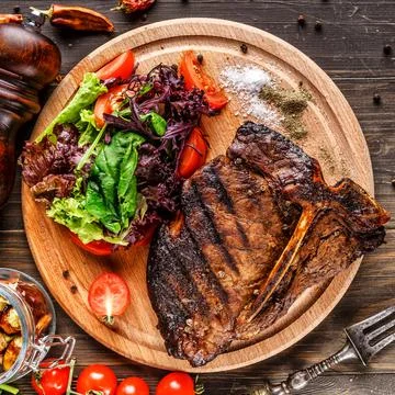 Beef T-Bone steak, herbs and spices on a dark table. Top view. Free space for Stock Photos