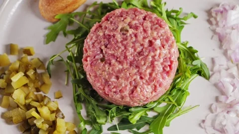 Beef tartare with arugula and capers, onions, bread slices and lime wedges on a Stock Footage 336060222