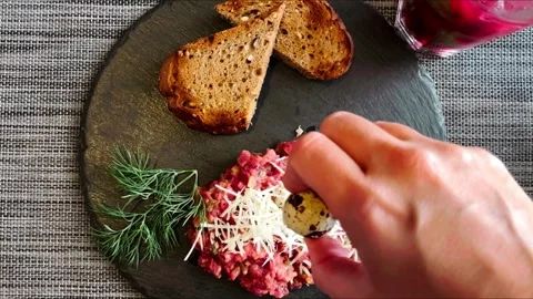 Beef tartare served on a plate with egg, bread and cheese. Hand close-up pouring Stock Footage 252371184