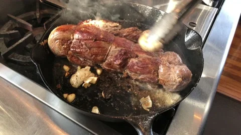 A beef tenderloin being cooked in a cast iron skillet on a stove top Stock Footage 123191482