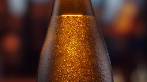 Beer bottle featuring lively bubbles and frothy foam, bar counter in background Stock Footage 257490223