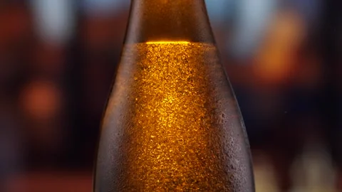 Beer bottle featuring lively bubbles and frothy foam, bar counter in background Stock Footage 259867050