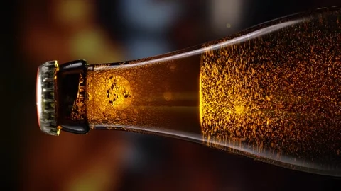 Beer bottle featuring lively bubbles and frothy foam, bar counter in background Stock Footage 261668565