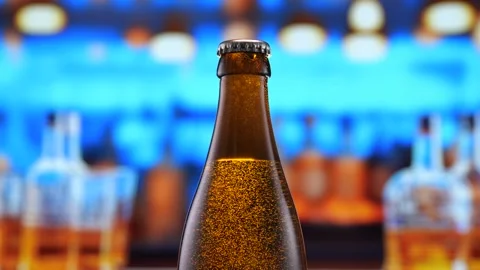 Beer bottle featuring lively bubbles and frothy foam, bar counter in background Stock Footage 275351544