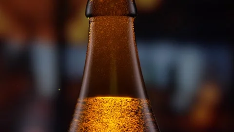 Beer bottle featuring lively bubbles and frothy foam, bar counter in background Stock Footage 275351562