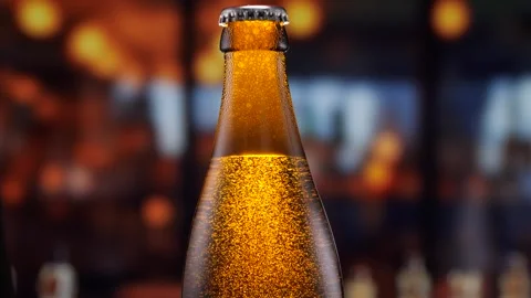 Beer bottle featuring lively bubbles and frothy foam, bar counter in background Video stock 276349469