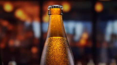 Beer bottle featuring lively bubbles and frothy foam, bar counter in background Stock Footage 278597307