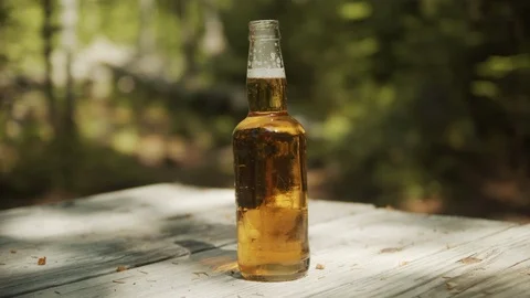 Beer Bottle Open and Bubbling on picnic table with forest background, 4k Video stock 111930093