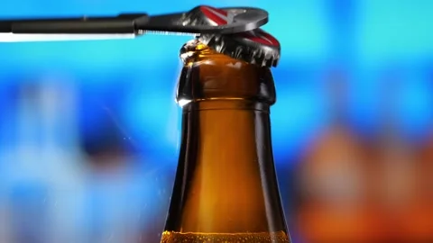 Beer bottle is opened with a bottle opener. Beer forms bubbles and a frothy Stock Footage 261947355