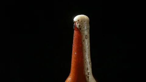 Beer foam pours from the neck of the bottle on a black background Stock Footage 117724441